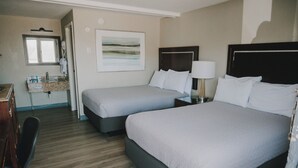 A hotel room with two beds, a bathroom with a sink and mirror, and a wooden floor.