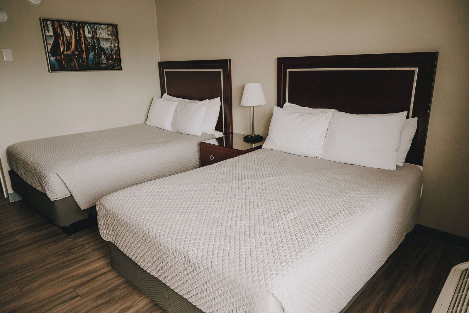 Two twin beds with wooden headboards, a bedside table with a lamp, and a painting on the wall.