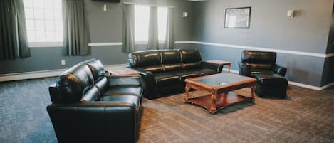 A room with a large window, a black leather sofa, a wooden coffee table, and a black leather armchair.