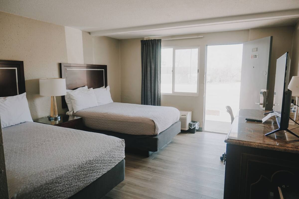 A hotel room with two beds, a desk, a chair, a television, and a window with curtains.