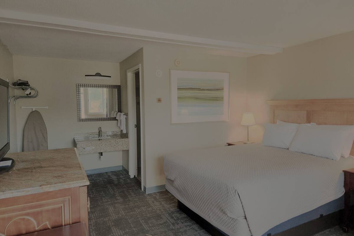A hotel room with a bed, bedside table, lamp, and a bathroom with a sink and mirror.