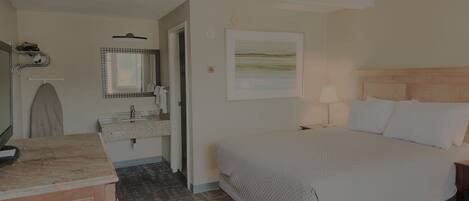 A hotel room with a bed, bedside table, lamp, and a bathroom with a sink and mirror.