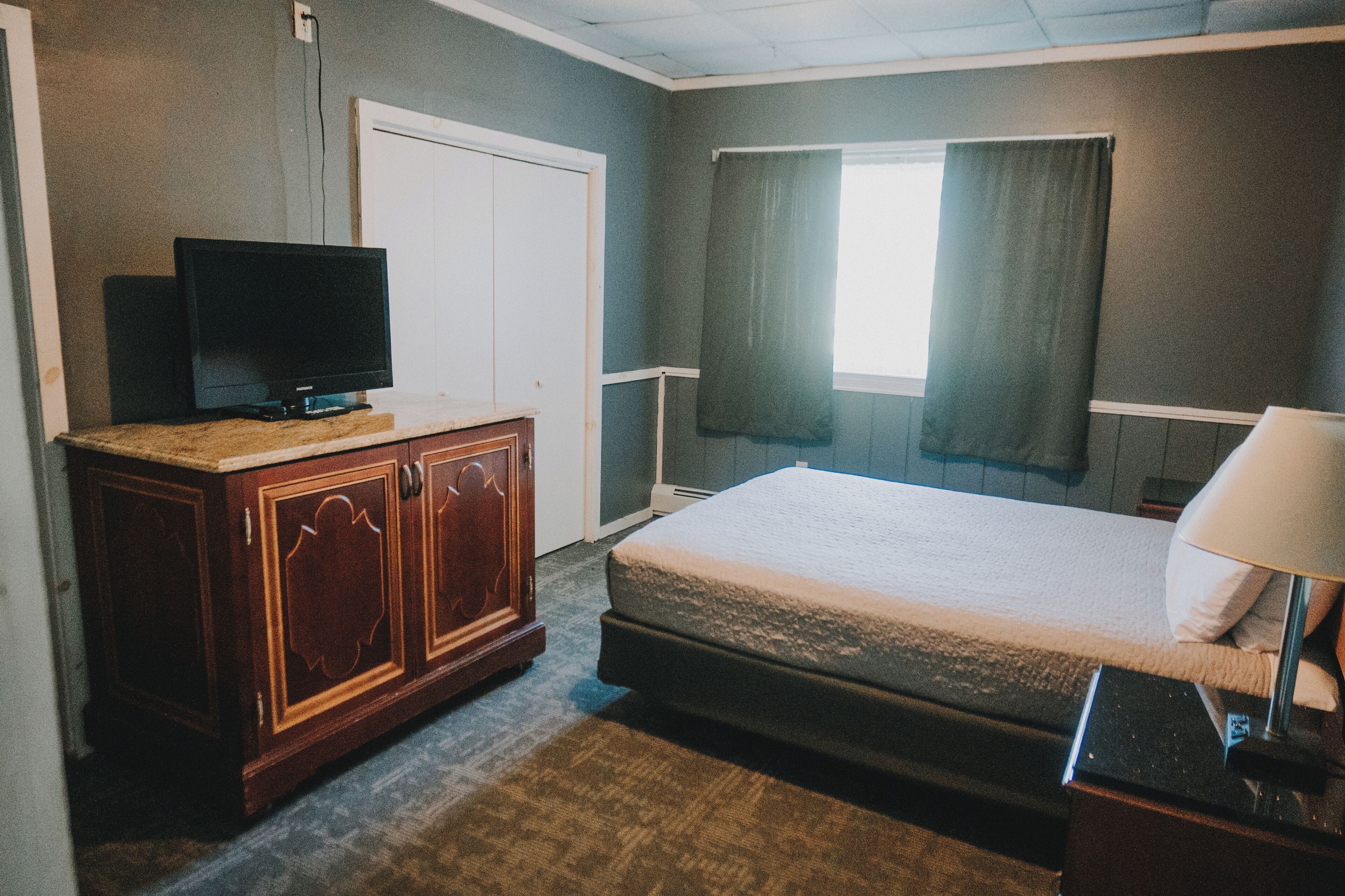 A hotel room with a bed, a wooden dresser, a television, and a window with curtains.
