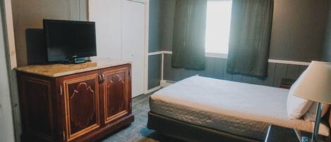 A hotel room with a bed, a wooden dresser, a television, and a window with curtains.