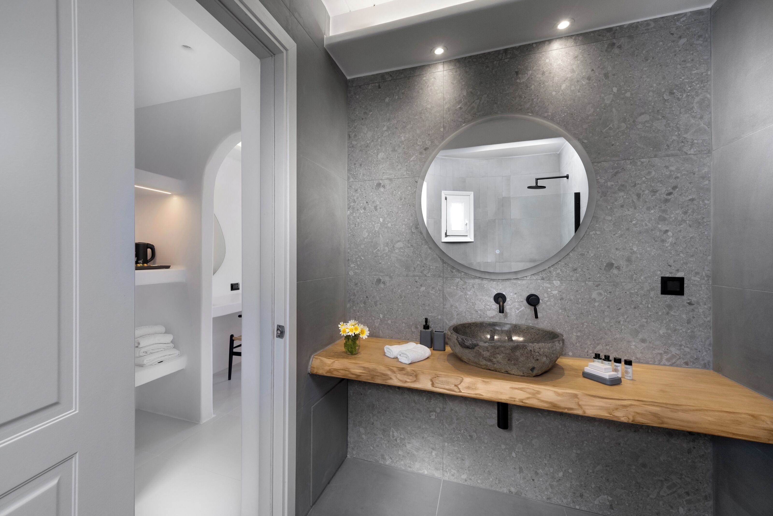 A modern bathroom with a round mirror, a stone sink, and a wooden countertop.