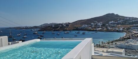 A clear blue pool with a view of boats on the sea and a hillside with white buildings.