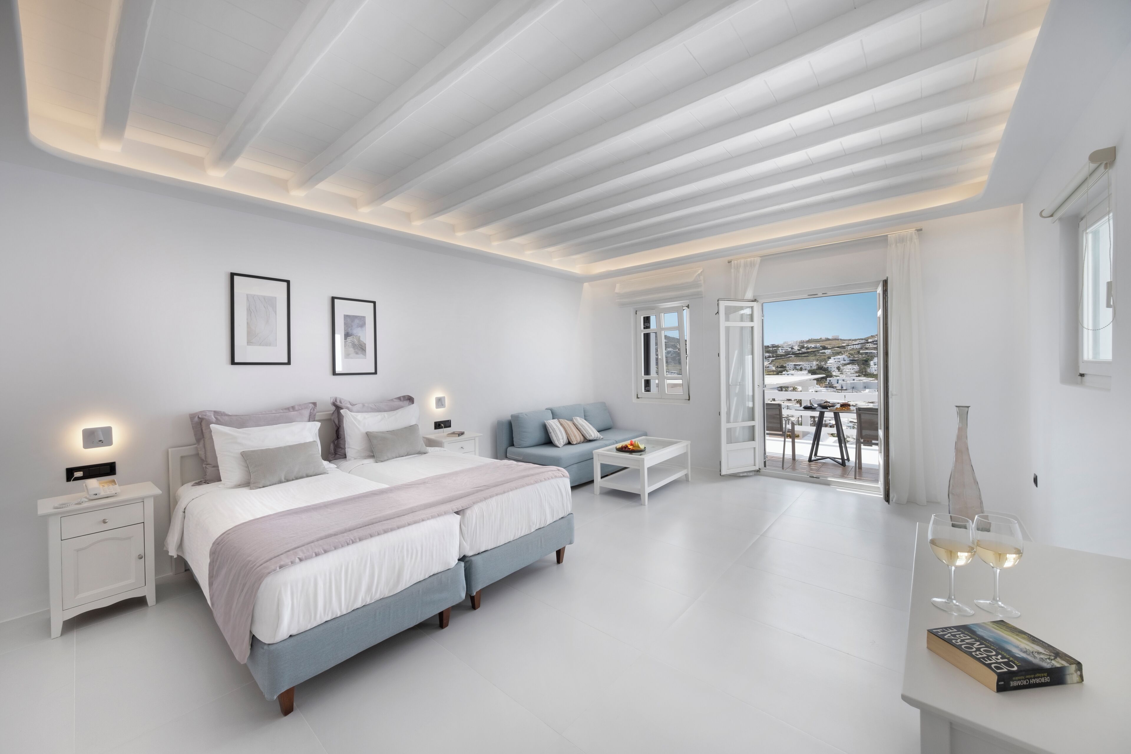 A modern bedroom with a large bed, bedside tables, a sofa, and a balcony with a view.