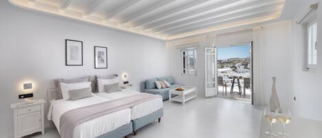 A modern bedroom with a large bed, bedside tables, a sofa, and a balcony with a view.