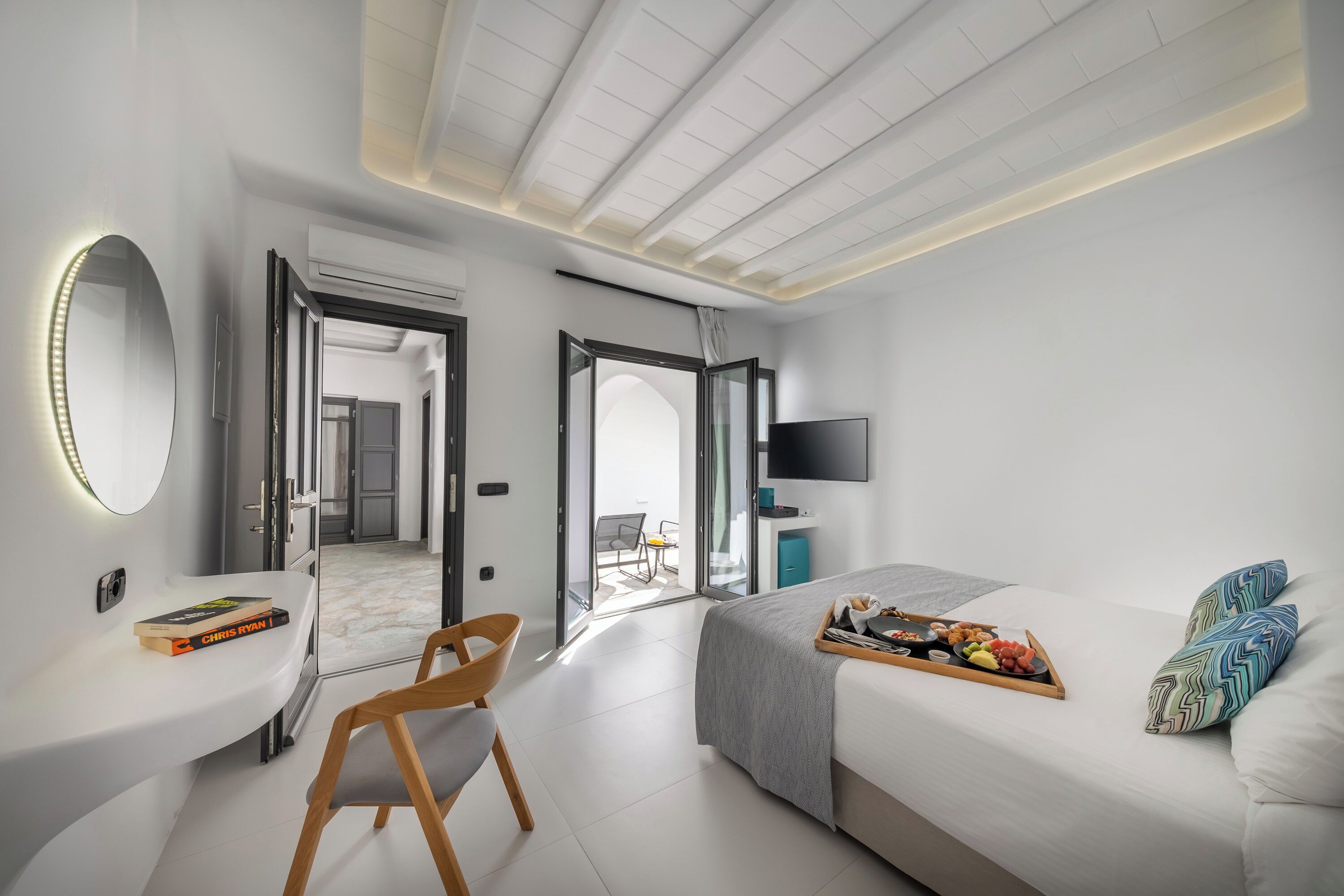 A modern hotel room with a bed, bedside table, chair, and a TV.