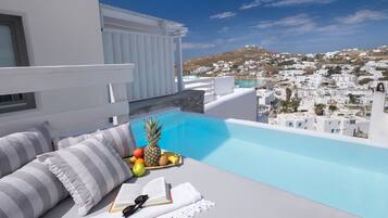 A rooftop lounge with a pool, white furniture, and a view of a white-washed town.