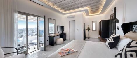 A modern bedroom with a large bed, a desk, and a balcony with a city view.