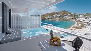 Un balcón con un jacuzzi, una cesta de frutas y vistas a una playa y edificios blancos.