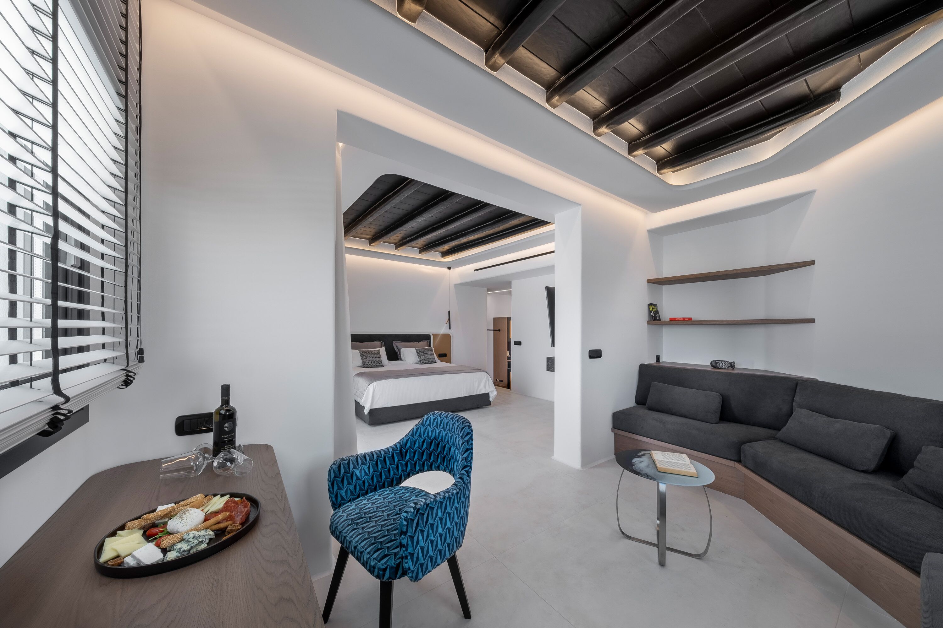 Une chambre d’hôtel moderne, équipée d’un lit, d’un canapé, d’un coin repas avec un plateau de collations et d’une chaise bleue.