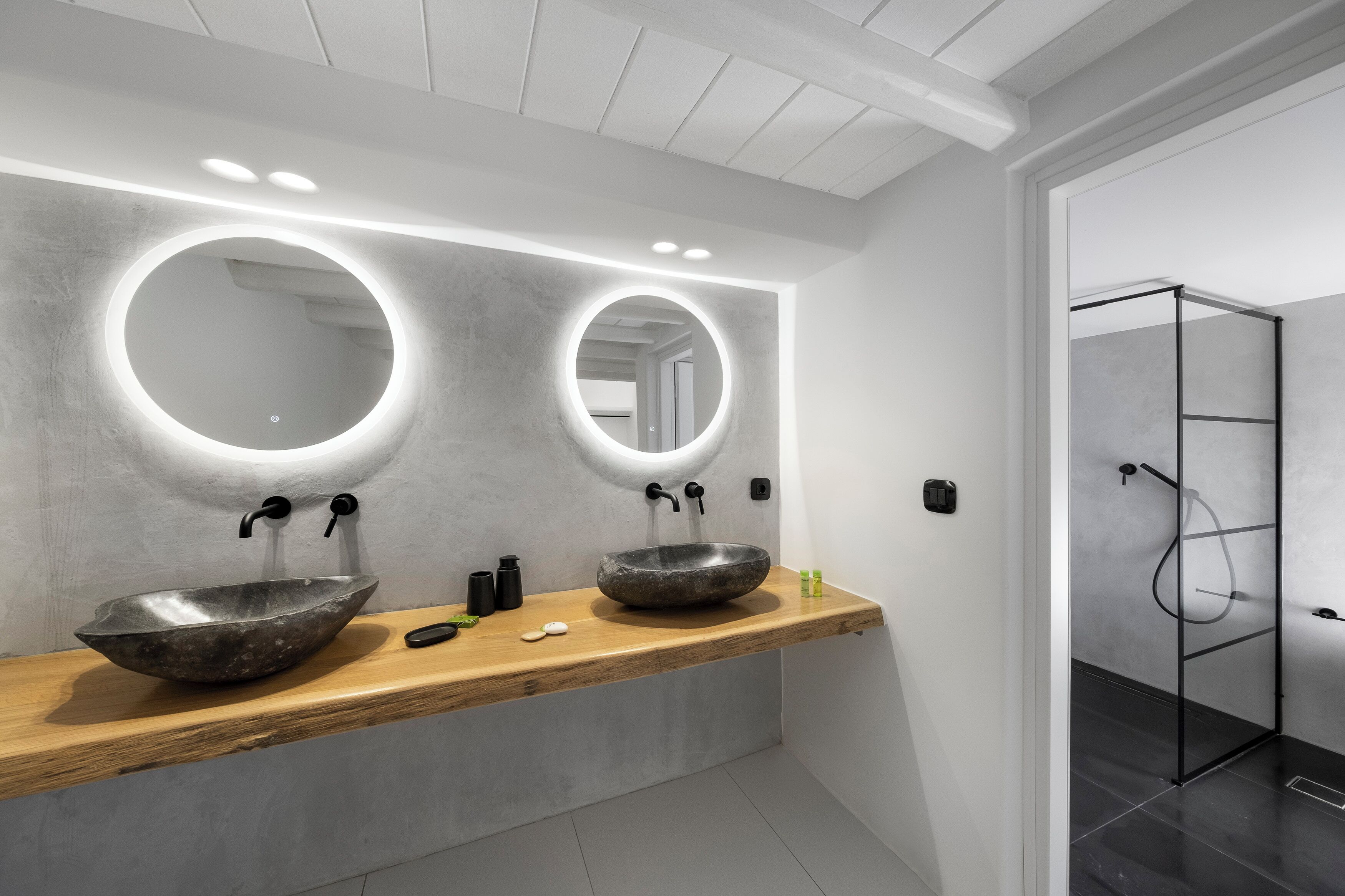 Un baño moderno con dos espejos redondos grandes, un tocador de madera y una ducha con mampara de vidrio.