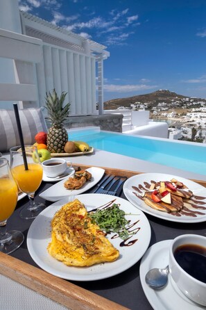 A breakfast setup with a view of a pool and a mountain in the background. - Deliades Mykonos (Mykonos)