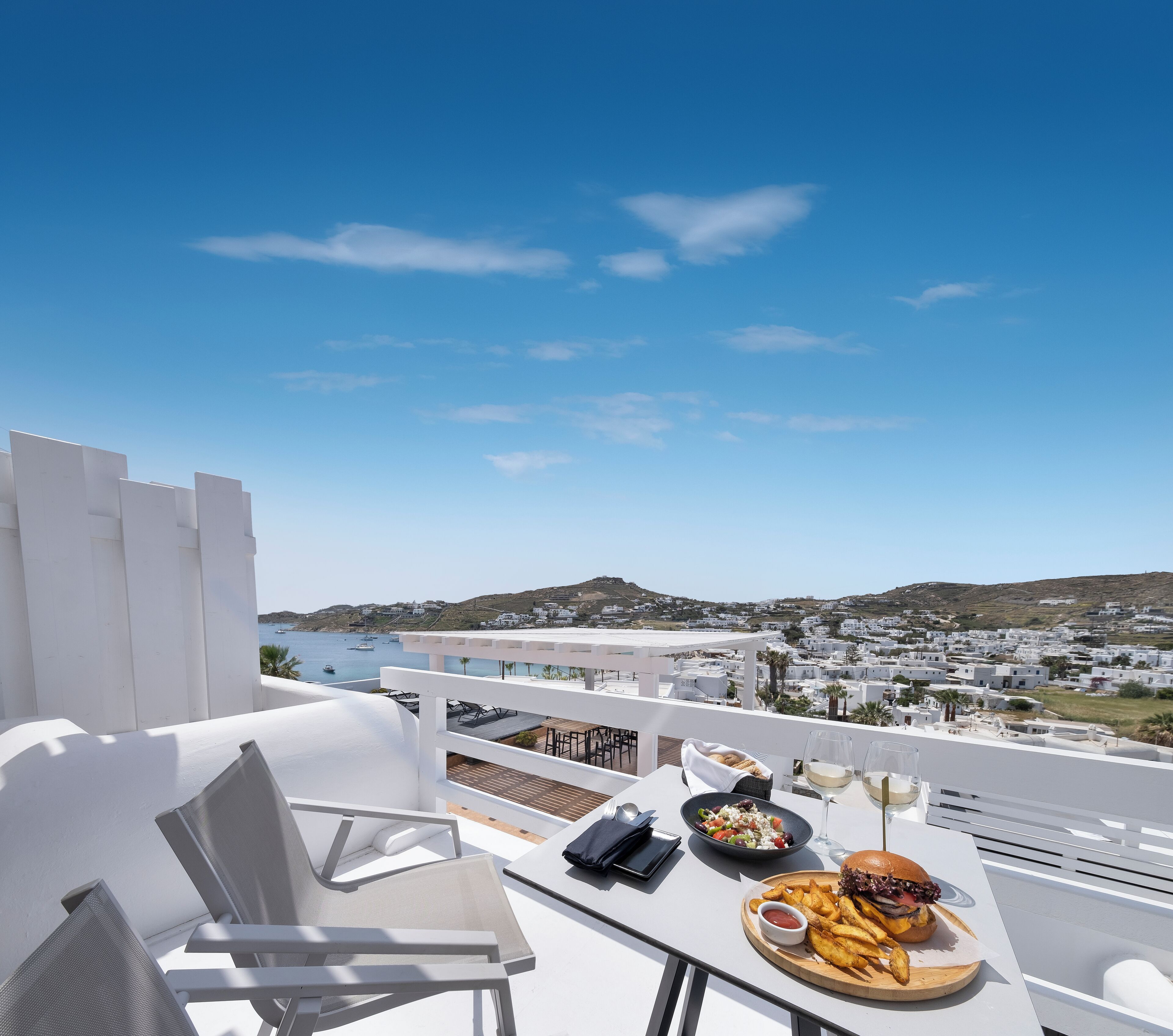 A terrace with a table set for a meal, overlooking a coastal town.
