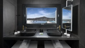 Un baño moderno con un amplio ventanal que ofrece vistas a un paisaje costero y una montaña.