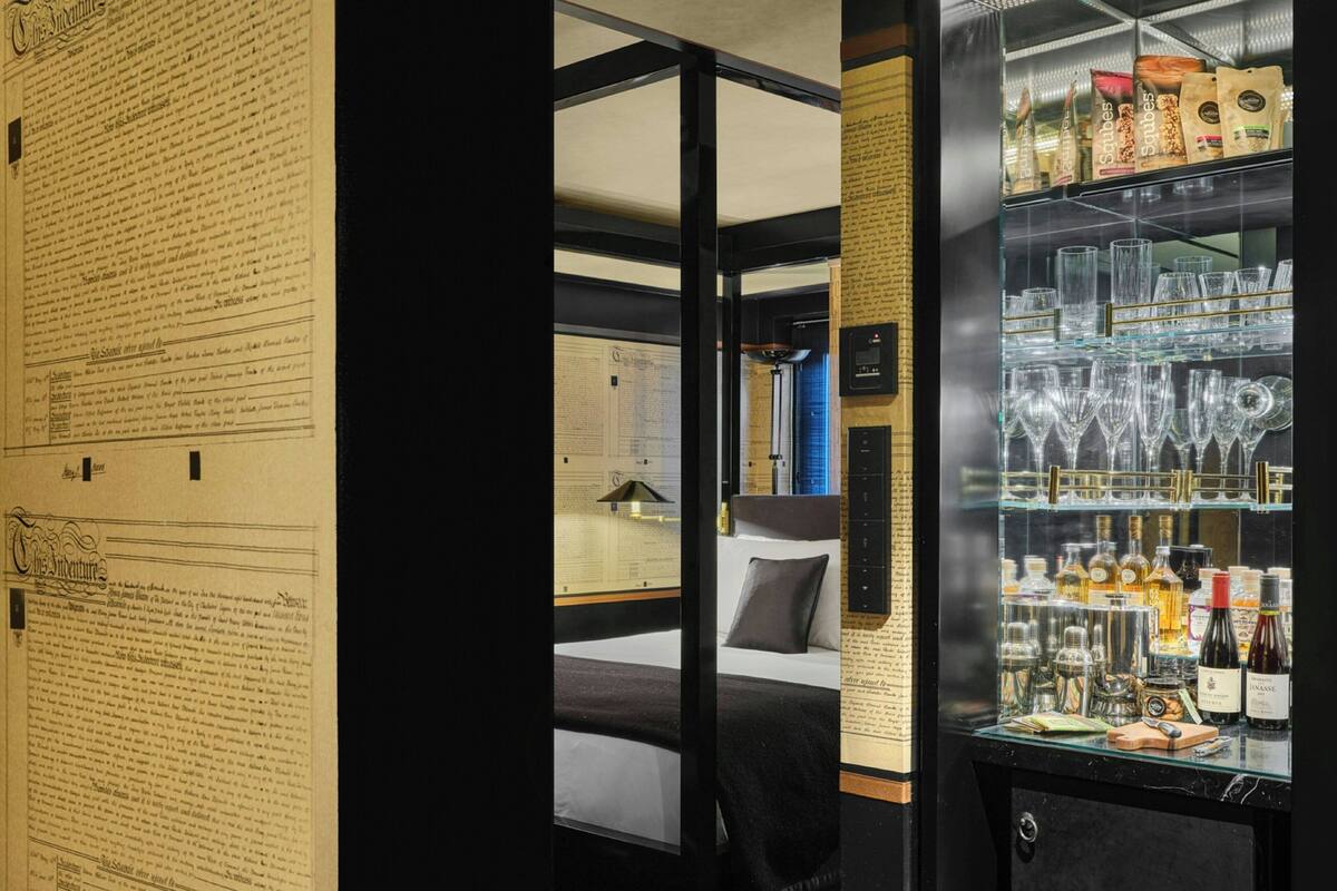 Une chambre d’hôtel avec un lit, une vitrine contenant des bouteilles et un mur avec du texte.