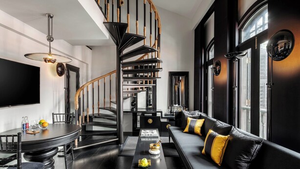A modern living room with a black and white color scheme, a spiral staircase, a black sofa with yellow cushions, and a dining area with a round table and chairs. - Duxton Reserve Singapore, Autograph Collection (Singapore)