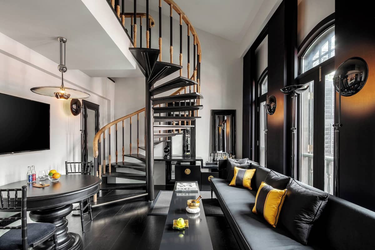 Un salon moderne aux couleurs contrastées, en noir et blanc, avec un escalier en colimaçon, un canapé noir agrémenté de coussins jaunes et un coin repas comprenant une table ronde et des chaises.
