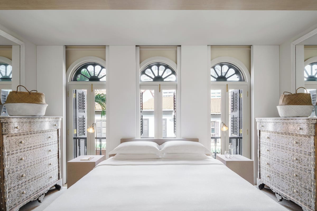 Une chambre à coucher avec un grand lit, deux commodes et trois fenêtres en arc de cercle.