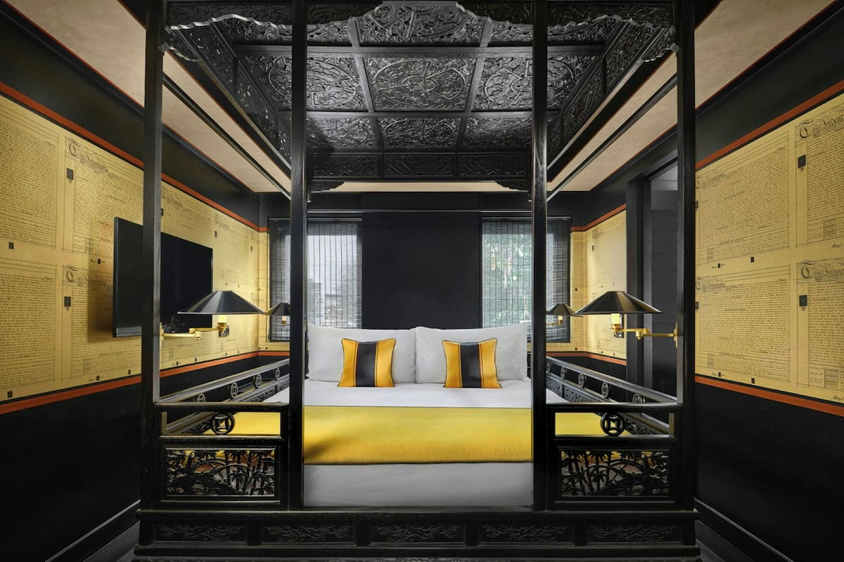 Une chambre à coucher luxueuse, dotée d’un grand lit, d’un plafond richement décoré et de panneaux muraux aux motifs élaborés.