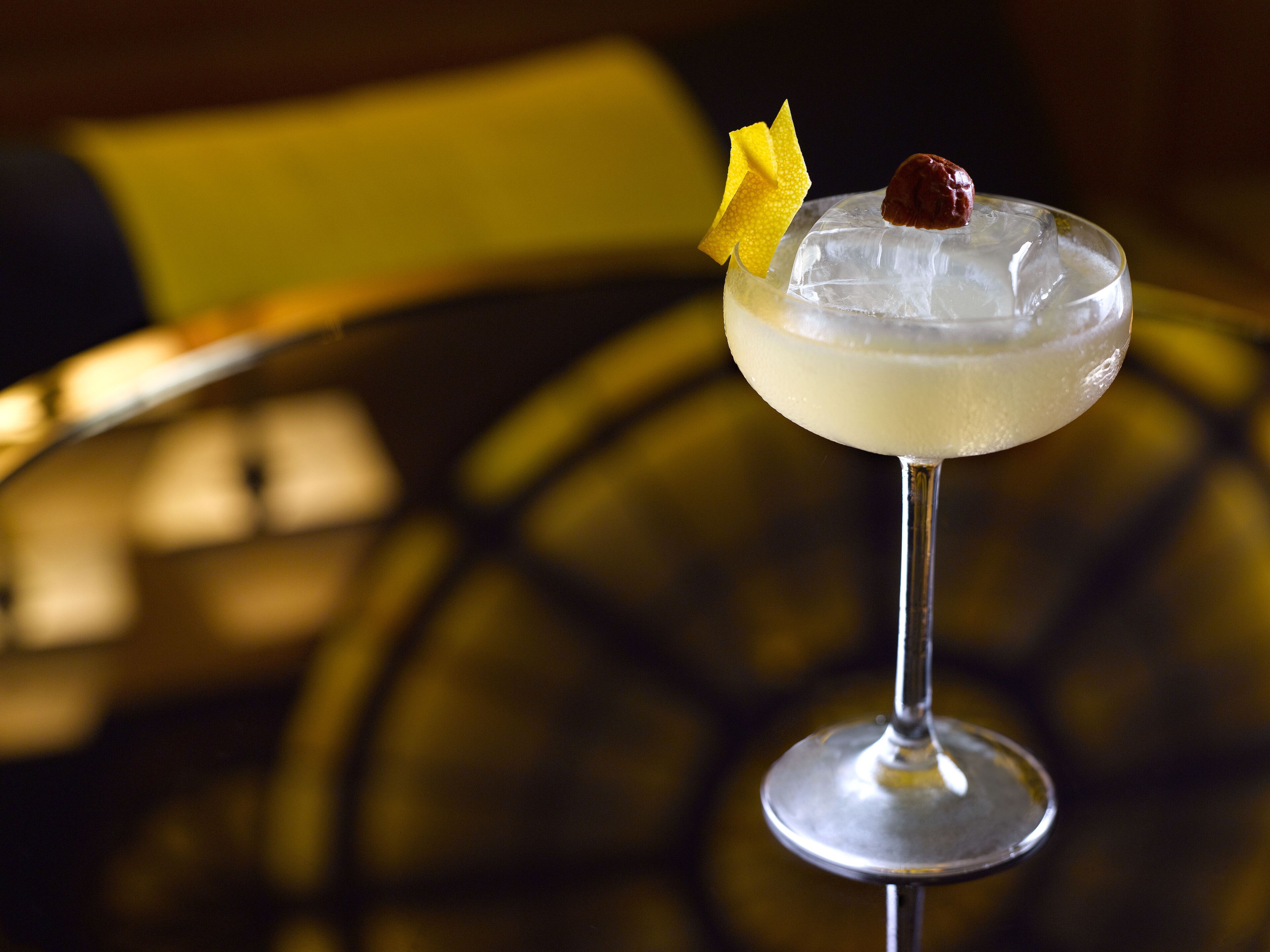 A cocktail in a stemmed glass with ice and garnishes on a reflective surface.