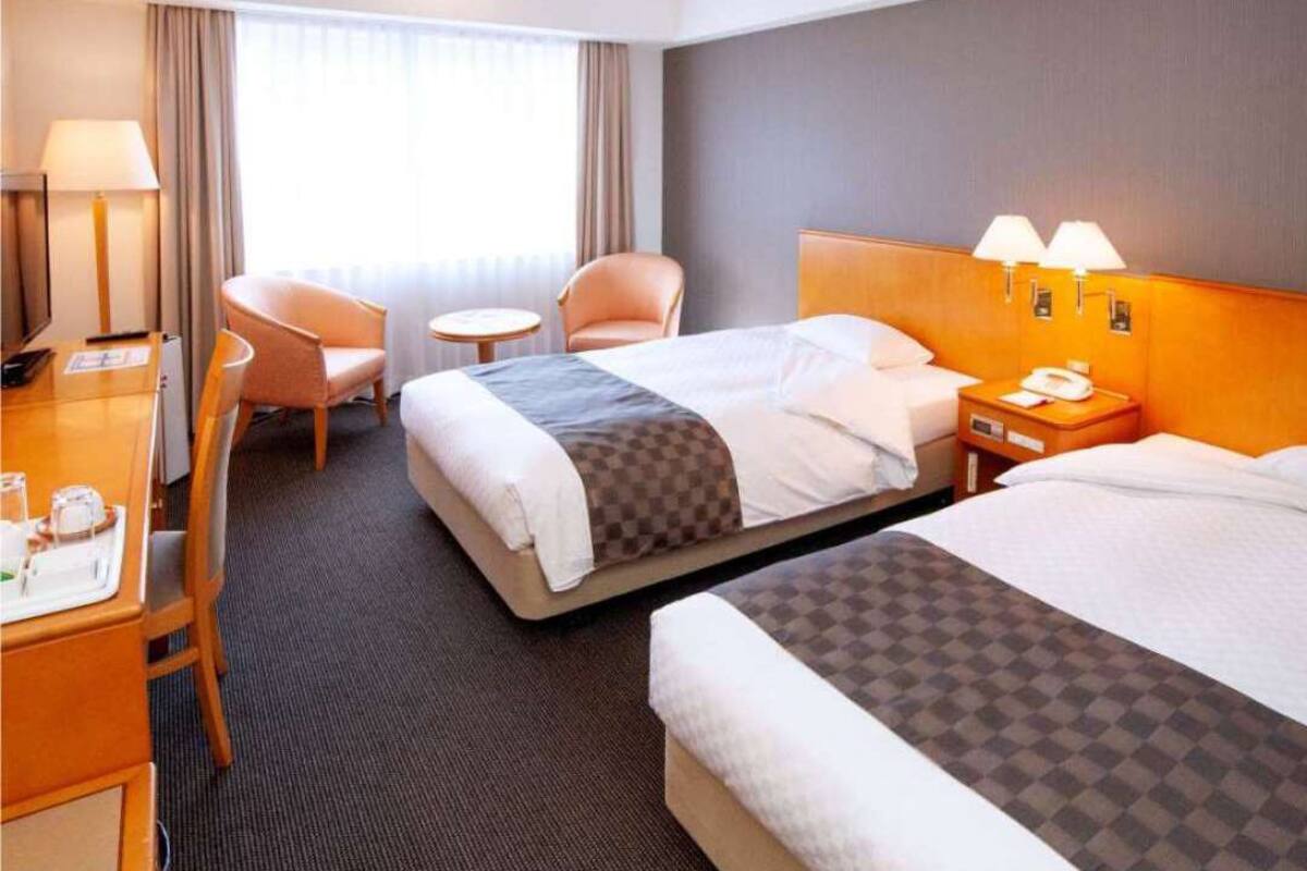 Habitación de hotel con dos camas, un escritorio con silla, una mesita redonda y una lámpara.