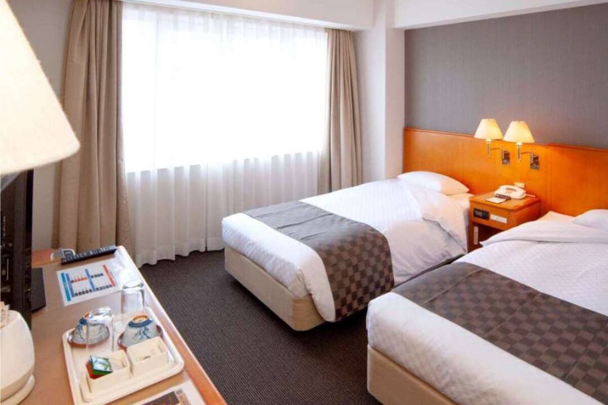 Habitación de hotel con dos camas, un escritorio con teléfono y una ventana con cortinas.