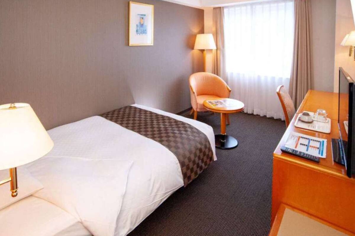Habitación de hotel con cama, escritorio, silla, lámpara y televisor.