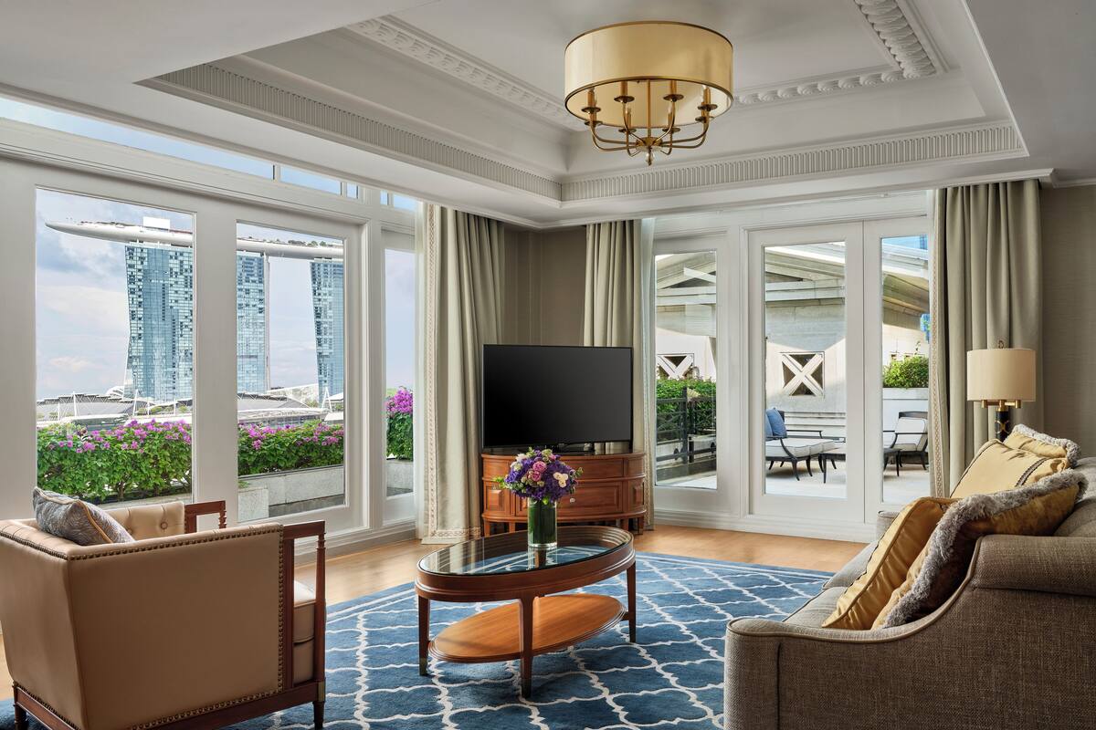 A spacious living room with a large TV, comfortable seating, a round coffee table, and a view of the cityscape through large windows.