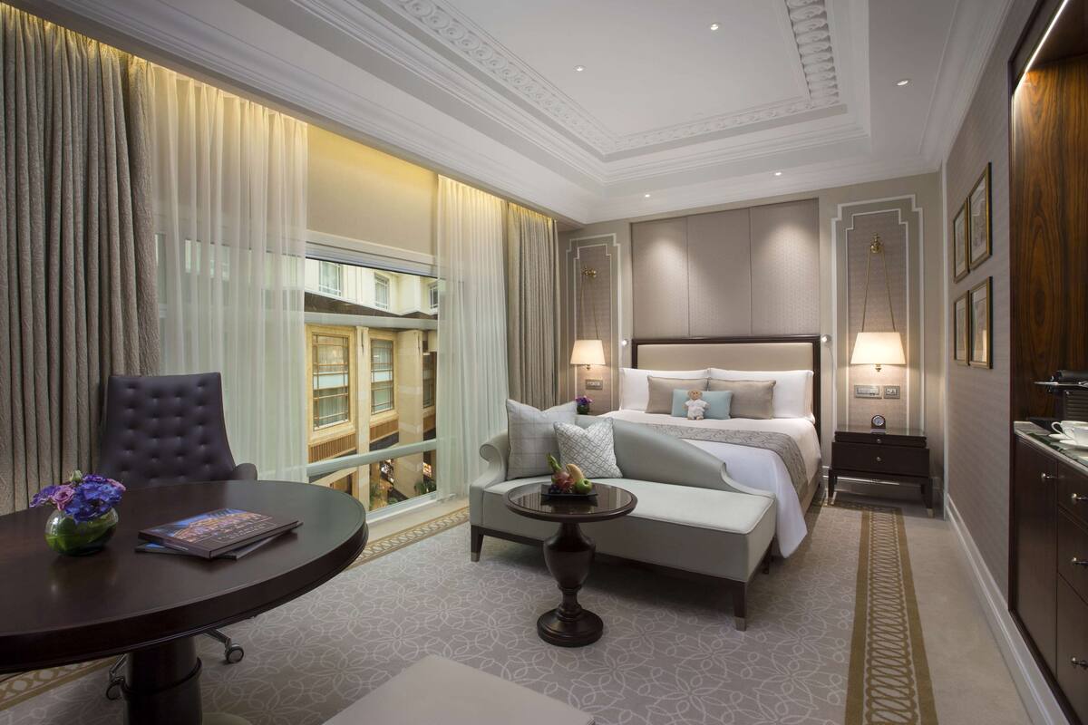 A hotel room with a bed, a sofa, a dining table, and a view of the city.