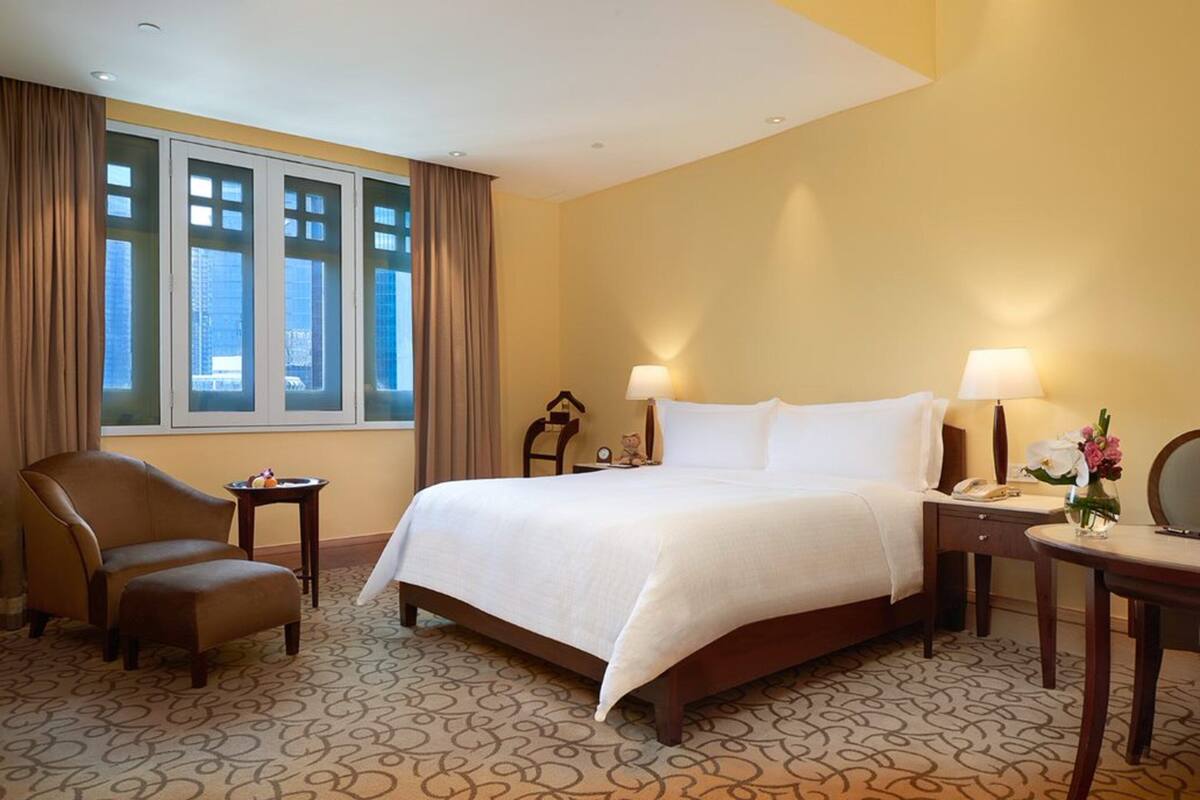 A hotel room with a large bed, two bedside tables, a chair, and a window with curtains.