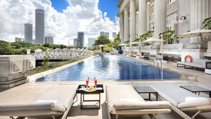 Piscina en la azotea con sillones y una mesa con bebidas, con vistas a un horizonte urbano y un puente.