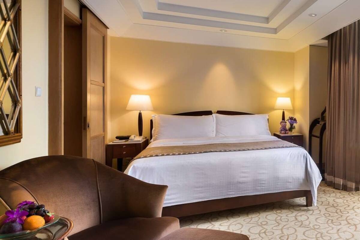 A hotel room with a large bed, two bedside lamps, a nightstand, a chair, and a fruit bowl.