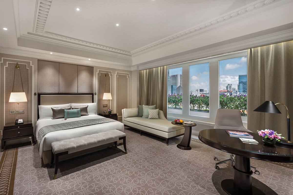 A hotel room with a large bed, a sofa, a desk, and a view of the city.