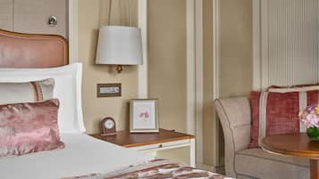 A hotel room with a bed, bedside table, lamp, clock, framed picture, and a sofa.
