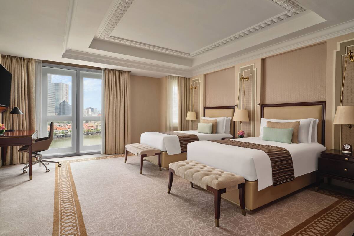 A hotel room with two beds, a desk, a chair, and a large window with curtains.