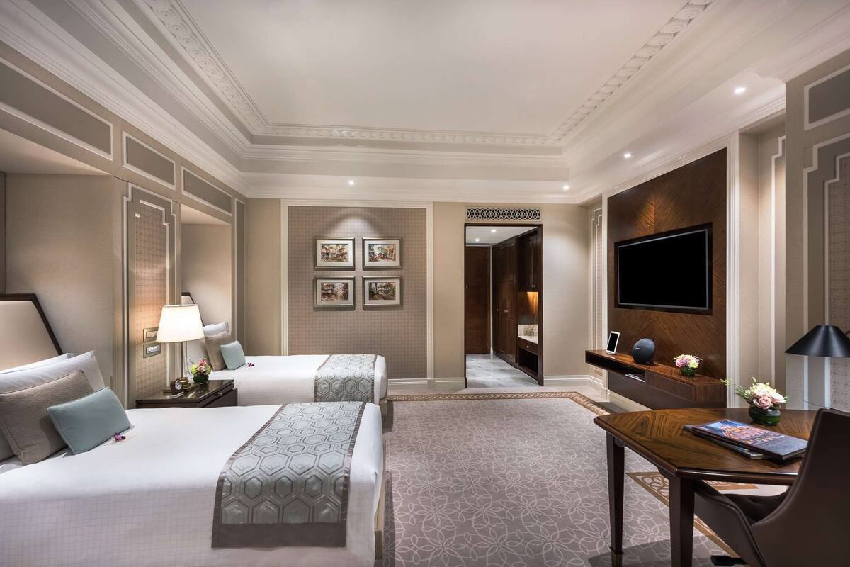 A hotel room with two beds, a desk, a TV, and a bathroom visible through an open door.