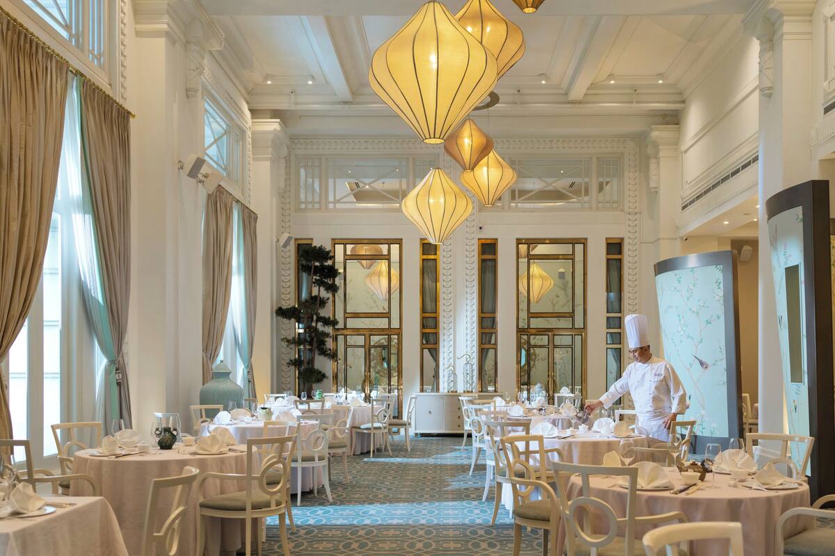 A formal dining room with round tables, white chairs, and chandeliers.