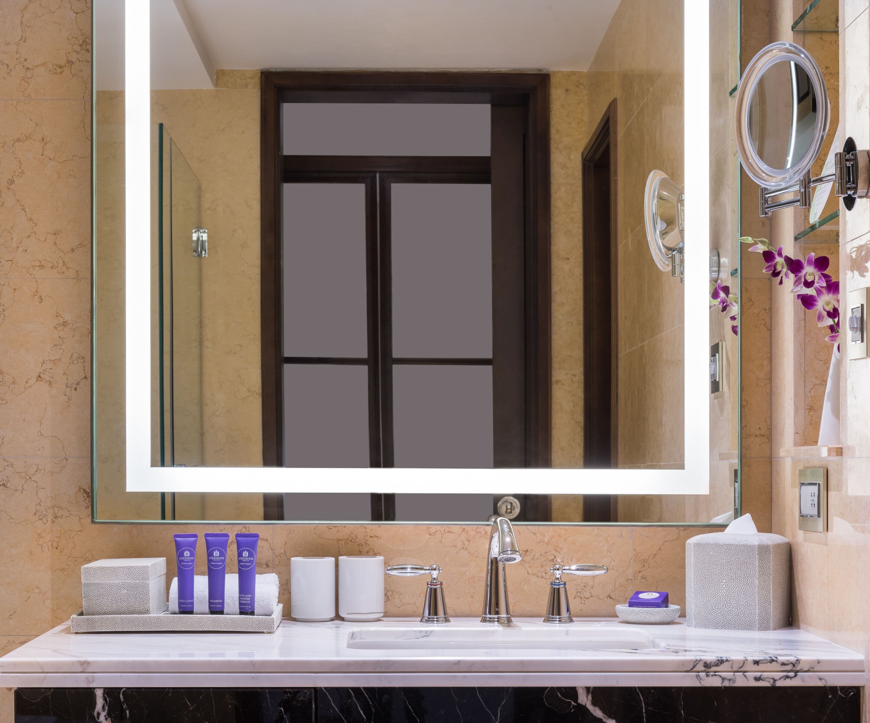 A bathroom with a large mirror, a sink with two faucets, and toiletries on the counter.