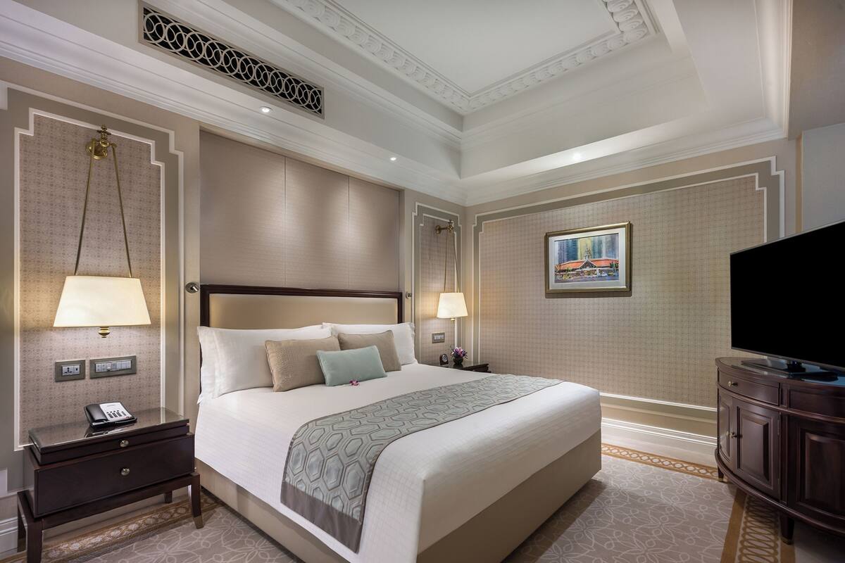 A hotel room with a large bed, bedside lamps, a nightstand, a television, and a framed picture on the wall.