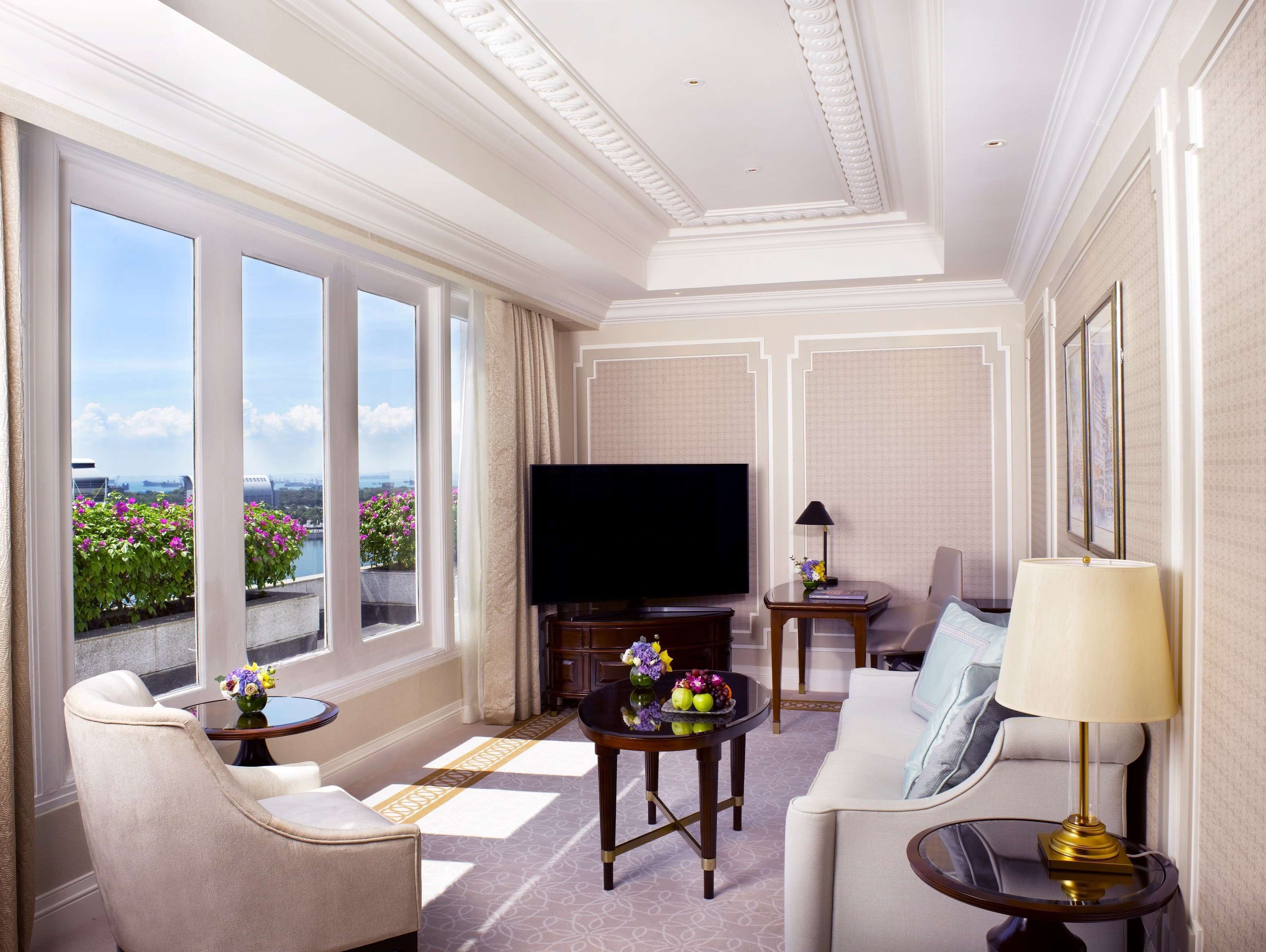A spacious living room with a large flat-screen TV, comfortable seating, and a view of the city through large windows.