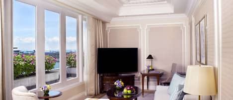 A spacious living room with a large flat-screen TV, comfortable seating, and a view of the city through large windows.
