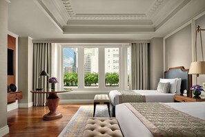 A hotel room with a large window, a bed, a bedside table, a lamp, and a small table with a vase of flowers. - The Fullerton Hotel Singapore (Singapore)