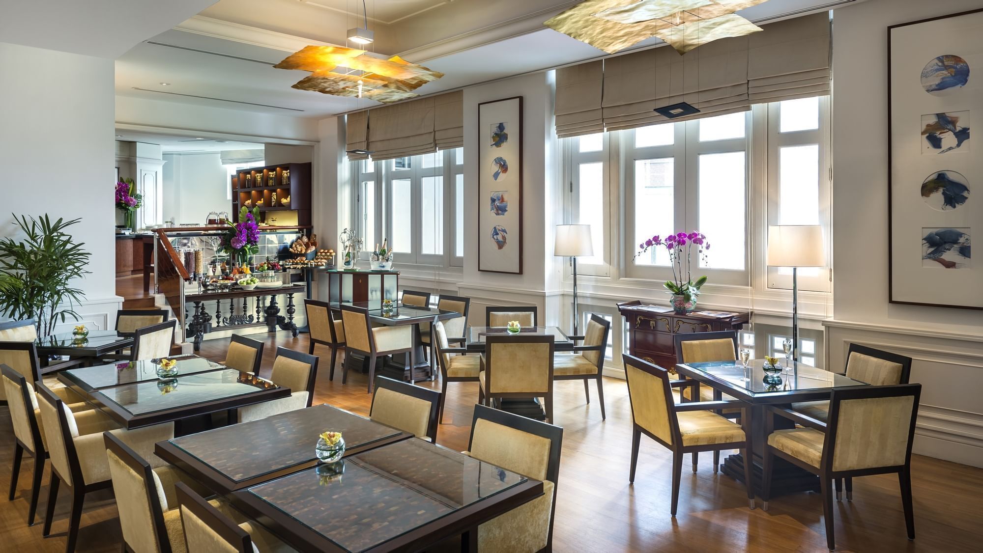 A spacious dining area with multiple tables and chairs, large windows with curtains, and a decorative ceiling light.