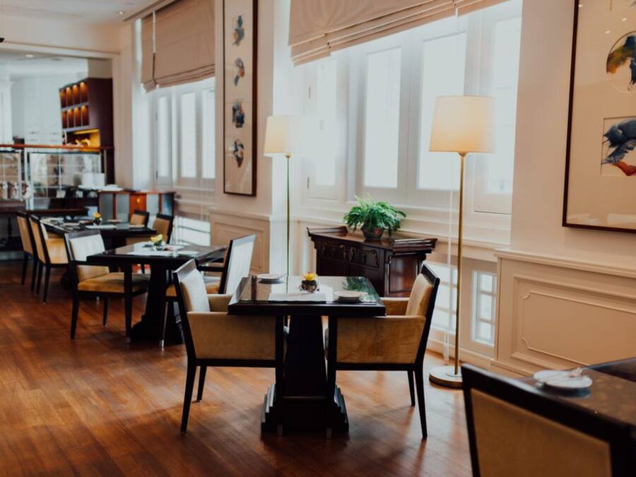 Un comedor con suelo de madera, mesas, sillas y un ventanal con persianas.
