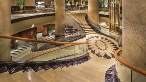 Un lobby de hotel elegante con una escalera de mármol, grandes columnas y un atrio central.