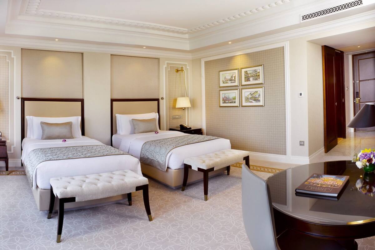 A hotel room with two beds, a sitting area, and a view of the city.