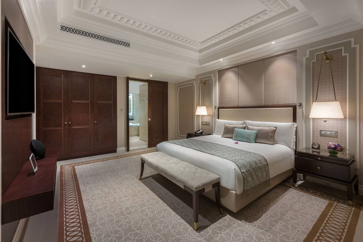 A spacious bedroom with a large bed, a bench, a desk, and a TV.